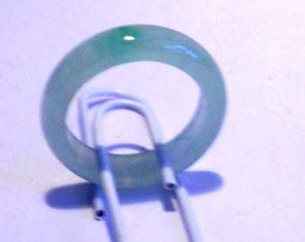 May include: A translucent, light green jade ring. The ring is circular and appears to be made of a single piece of jade. The ring is resting on a white paperclip, casting a shadow on the white surface.