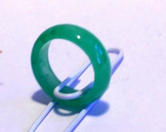 May include: A vibrant green jade ring, circular in shape, is the focal point. The ring is resting on a white paperclip, creating a contrast. The jade has a glossy finish, reflecting light. The background is a soft, off-white surface.