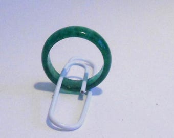 May include: A smooth, solid green band ring with a polished finish. The ring is positioned upright, resting against a white metal paperclip, showcasing its circular shape and consistent, vibrant green color throughout the band.