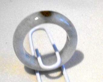 Puede incluir: Un brazalete de jade gris translúcido. El brazalete circular tiene una sutil variación de color y un acabado pulido. El jade está sobre un clip blanco.