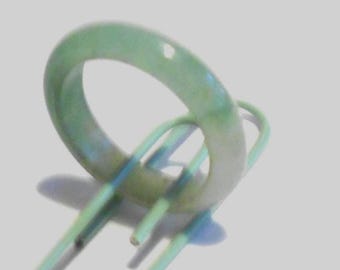 May include: A light green jade ring. The ring is a solid band with a smooth, polished surface. The jade has subtle variations in color, with hints of blue and white. The ring is displayed on a light green and blue object.