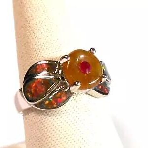 May include: A silver ring with a large yellow opal gemstone set in a silver setting. The opal has a red stone in the center. The ring is set with smaller opals on the band.