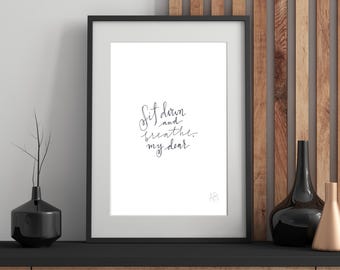 May include: A black framed print with white background and black calligraphy that reads "Sit down and breathe, my dear". The print is on a wooden shelf with black vases.