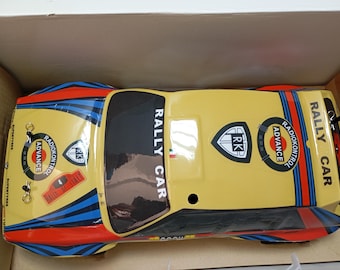 May include: A yellow and black toy rally car with blue and red stripes. The car has the words "RALLY CAR" and "RADIOKONTROL ADVANCE" printed on it. The car is in a cardboard box.