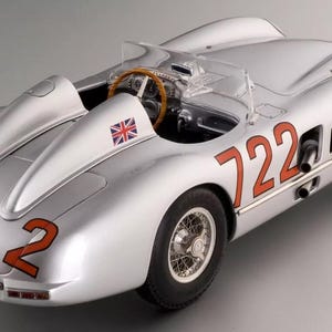 May include: Silver vintage race car model with the number 722 in orange on the side and rear. The car features a Union Jack flag and a wooden steering wheel. The model has detailed wheels and a clear windscreen.