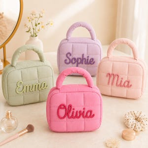 May include: Four small, quilted, rectangular cosmetic bags with top handles in sage green, lavender, light pink, and bright pink. Each bag features a name embroidered in a matching rope-style script: Emma, Sophie, Mia, and Olivia.