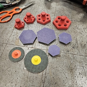 May include: Assortment of sanding discs and red plastic sanding blocks. The sanding discs are various sizes and have different grit levels. The sanding blocks are hexagonal shaped with a small knob on top.
