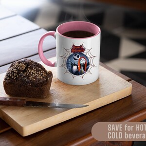 May include: A white mug with a pink interior and handle, featuring a Halloween-themed graphic of Jack Skellington and Sally. The mug is on a wooden cutting board with a slice of bread and a knife. The mug is filled with a dark liquid.