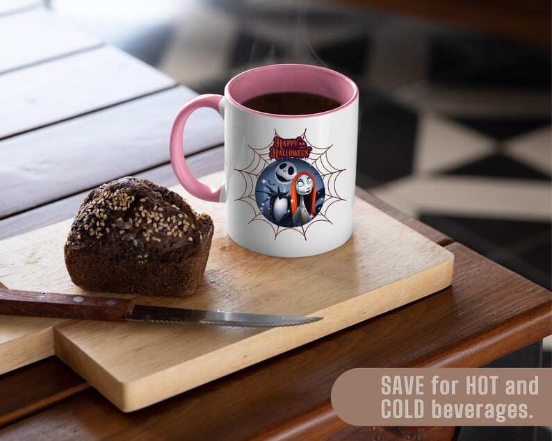 May include: A white mug with a pink interior and handle, featuring a Halloween-themed graphic of Jack Skellington and Sally. The mug is on a wooden cutting board with a slice of bread and a knife. The mug is filled with a dark liquid.