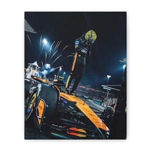 May include: A canvas print featuring a Formula 1 race car in orange and black, with a driver standing on top. The driver is wearing a yellow and black helmet and racing suit. Fireworks are in the background.