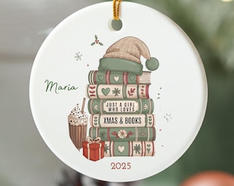 Puede incluir: Adorno navideño redondo de cerámica con una pila de libros coronada por un gorro de Papá Noel. El adorno presenta el texto "Just a girl who loves Xmas & Books" y el año 2025. También se representa una bebida de café y una caja de regalo.