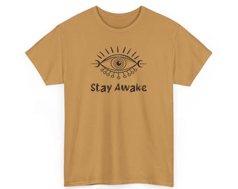 Puede incluir: Una camiseta de color amarillo mostaza con un gráfico en blanco y negro de un ojo con el texto "Stay Awake" debajo.