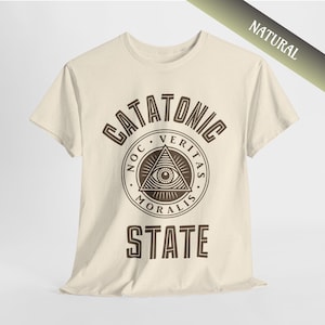 May include: A beige t-shirt with a brown graphic print of a triangle with an eye inside. The text "CATATONIC STATE" is printed above and below the graphic. The text inside the triangle reads "NOC VERITAS MORALIS".