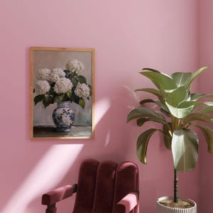 Puede incluir: Una pintura enmarcada de un ramo de hortensias blancas en un jarr&oacute;n de porcelana azul y blanco sobre un fondo gris claro.