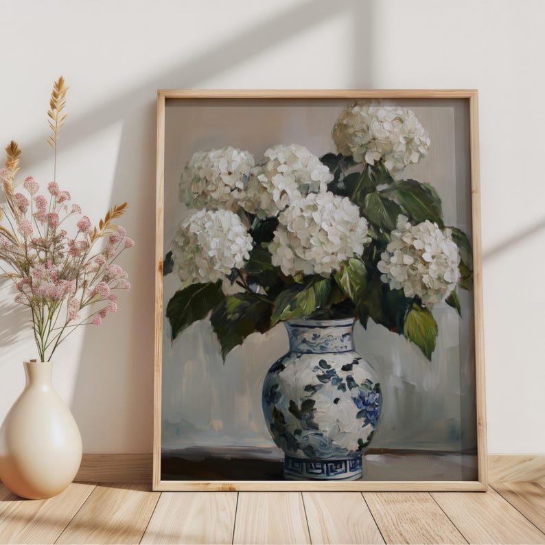 Puede incluir: Una pintura de un ramo de hortensias blancas en un jarr&oacute;n de porcelana azul y blanco. El jarr&oacute;n tiene un patr&oacute;n floral y est&aacute; sobre una mesa de madera.