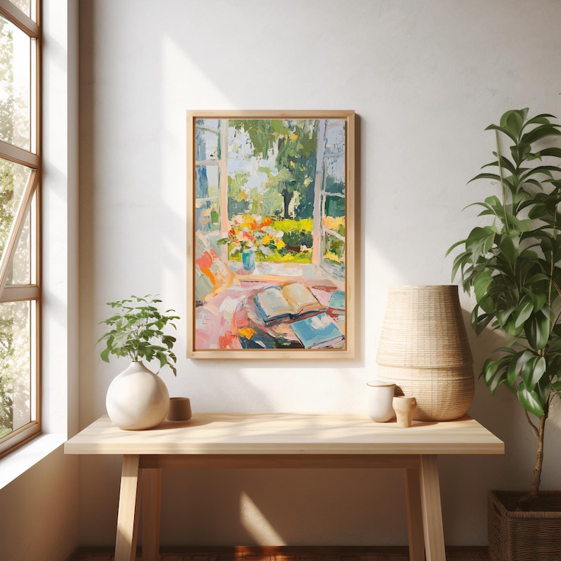 May include: A framed painting depicting a window with a view of a garden. The window is open and there are books on a table in front of it. The painting is in a light wood frame and is hanging on a white wall.