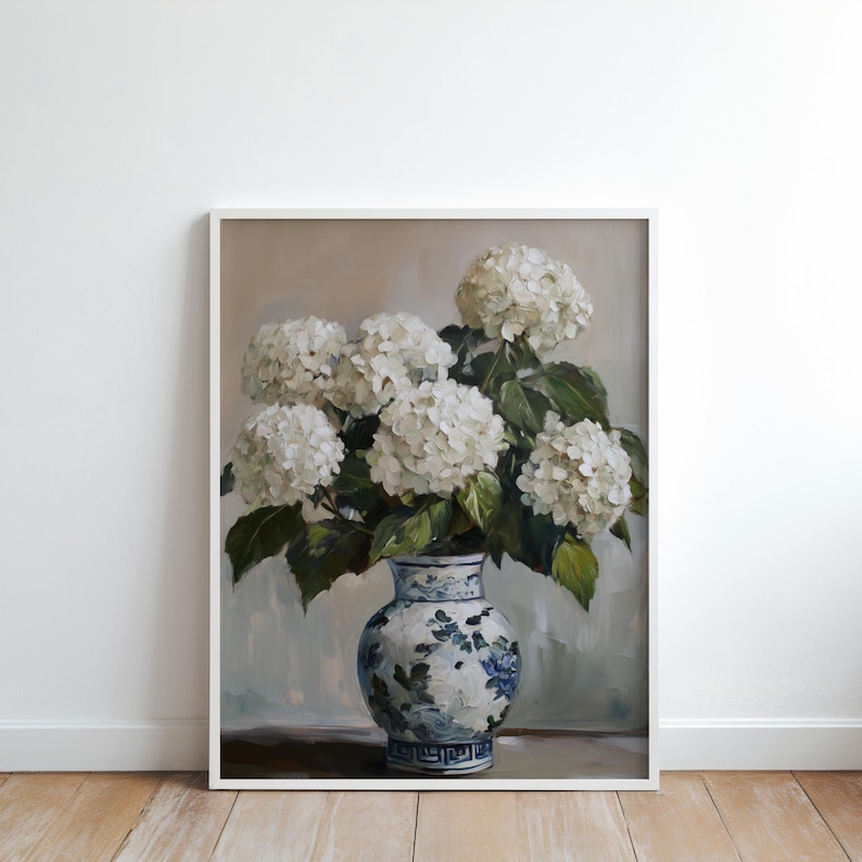 Puede incluir: Un jarr&oacute;n de porcelana blanca con dise&ntilde;os florales azules y blancos contiene un ramo de hortensias blancas. El jarr&oacute;n est&aacute; sobre una superficie de madera.