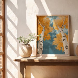 May include: A framed print of two birch trees with yellow leaves against a blue sky. The trees are reaching up towards the sky, and the leaves are a vibrant yellow.