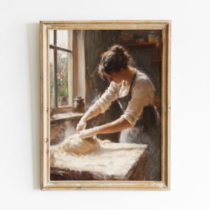 Könnte beinhalten: Gerahmtes Vintage-Gemälde, das eine Frau beim Kneten von Teig in einer Küche zeigt. Sie trägt ein weißes Hemd und eine dunkle Schürze. Die Szene wird von einem Fenster beleuchtet, mit einem warmen, goldfarbenen Rahmen. Das Kunstwerk erinnert an häusliches Leben und traditionelles Backen.