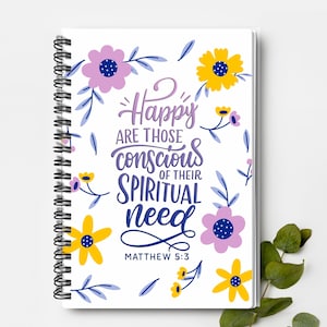 May include: A spiral-bound notebook with a white cover featuring the text "Happy are those conscious of their spiritual need" and the reference Matthew 5:3. The design includes purple and yellow flowers with blue leaves.