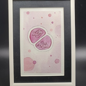May include: A framed watercolor painting of two pink, round shapes with swirling lines inside. The background is a light pink with scattered pink dots.