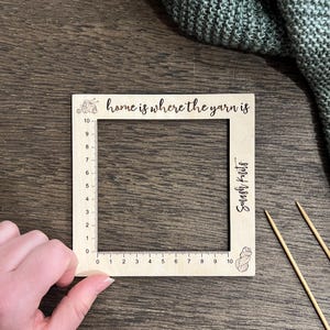 May include: A wooden yarn gauge with a square frame and etched measurements from 0 to 25 cm. The text "home is where the yarn is" is above the frame. The gauge also has the text "Smash Knits".