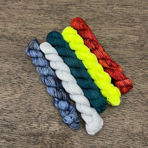 May include: A set of six mini skeins of yarn in various colors, including blue, green, white, yellow, and red. The skeins are arranged in a rainbow pattern.