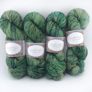 Peut inclure: Trois écheveaux de fil vert avec des reflets bruns. Chaque écheveau est étiqueté "Smash Krits Fibre Goods".