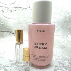 May include: A pink Berry Cream hair and body fragrance mist bottle with a white cap, and two small glass perfume bottles with gold caps. The large bottle reads "PHLUR BERRY CREAM HAIR & BODY FRAGRANCE MIST 8.1 Fl. Oz. (240 mL)".