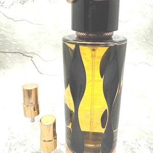 May include: A perfume bottle with a black and gold design, topped with a snake-shaped cap. Two small, gold-capped vials are next to the bottle. The perfume has a golden hue, and the bottle has a decorative pattern.