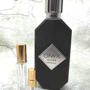 May include: A black Onyx Silver Khadlaj perfume bottle with a silver cap and a textured design. Two smaller clear glass bottles with gold caps are in front of the perfume bottle.
