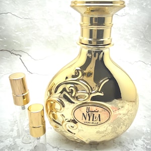 May include: A gold-colored perfume bottle with a decorative design and two smaller spray bottles. The perfume bottle has a rounded shape with a gold cap and the text "NYLA VANI-ELLE". The smaller bottles are clear glass with gold caps.