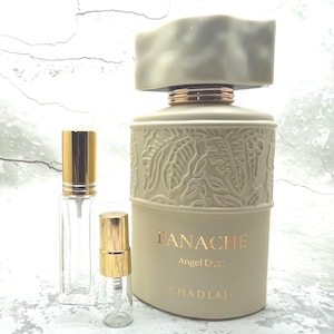 May include: A beige perfume bottle with a textured, light gray cap and gold accents. The bottle is labeled "PANACHE Angel Dust" and is accompanied by two smaller, clear glass spray bottles with gold caps. The design features embossed leaf patterns.