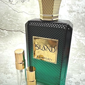 May include: A dark green perfume bottle with a gold cap and a gold label that reads "ISLAND KHADLAJ." Two small, clear spray bottles with gold caps are in front of the perfume bottle. The perfume bottle has a textured design.