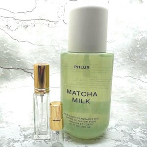 May include: A green bottle of PHLUR Matcha Milk hair and body fragrance mist, with two smaller glass spray bottles with gold caps. The large bottle has the text "Matcha Milk" and "Hair & Body Fragrance Mist".