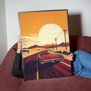 May include: A framed art print featuring a vintage red convertible driving down a desert highway at sunset. The artwork has a retro style with a large sun, mountains, and power lines. The color palette includes shades of red, orange, and brown.