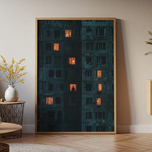 May include: Framed art print of a dark teal apartment building with several lit windows. A single figure is visible in one window. The artwork is in a wooden frame and is displayed indoors.