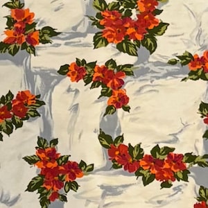 Op de afbeelding: Witte stof met een herhalend patroon van rode en groene bloemenontwerpen. De bloemen zijn gestileerd en hebben een vintage uitstraling.