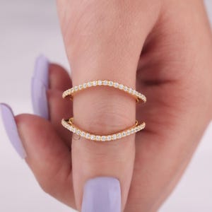 May include: A gold ring with two bands of small, clear stones. The bands are curved and meet at the top of the ring.