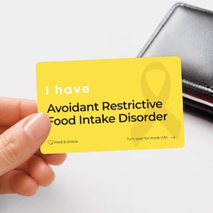May include: A rectangular yellow medical alert card with rounded corners. The text reads I have Avoidant Restrictive Food Intake Disorder. It features a yellow awareness ribbon graphic, the Med & Grace logo, and the text Turn over for more info.