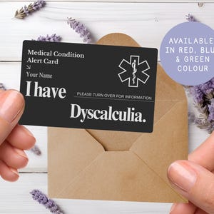 May include: A black medical alert card with white text and a medical symbol. The card reads "I have Dyscalculia." and "Medical Condition Alert Card." A purple circle states "Available in Red, Blue & Green Colour."