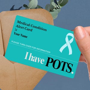 Peut inclure: Une carte d'alerte médicale bleu turquoise avec le texte "Medical Condition Alert Card" et "I have POTS." Un ruban bleu clair se trouve dans le coin supérieur droit. La carte est tenue par une main.
