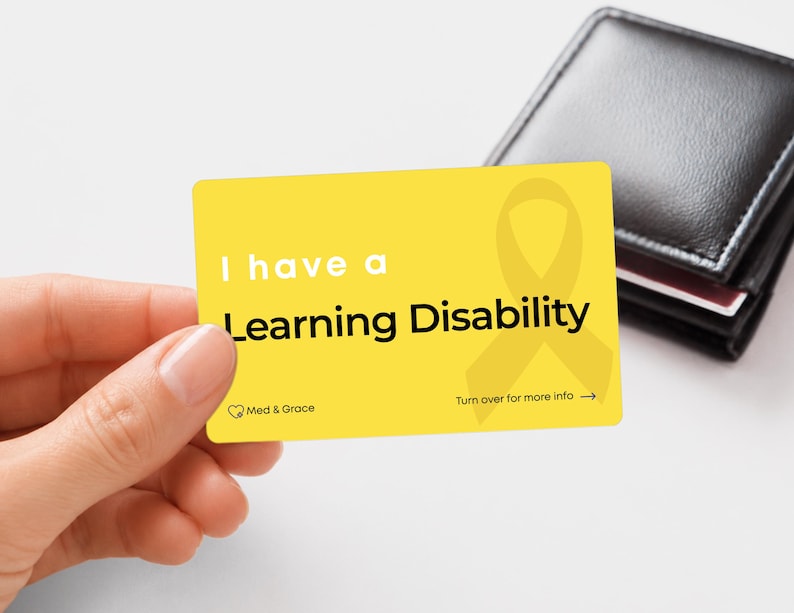 May include: A rectangular yellow identification card with rounded corners featuring the white and black text I have a Learning Disability, a yellow ribbon icon, the Med & Grace logo, and the text Turn over for more info with an arrow.