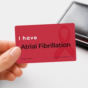 May include: A rectangular red medical alert card with rounded corners featuring the white and black text I have Atrial Fibrillation, a red awareness ribbon graphic, the brand name Med & Grace, and the text Turn over for more info with an arrow.