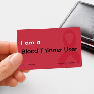 May include: A rectangular red medical alert card with rounded corners. The text reads I am a Blood Thinner User in white and black lettering. A red awareness ribbon is printed on the right side. The bottom includes Med & Grace and Turn over for more info.