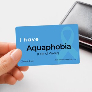 May include: A rectangular blue card featuring a light blue awareness ribbon and the white and black text: I have Aquaphobia (Fear of Water). The card includes the Med & Grace logo and the text Turn over for more info with an arrow pointing right.