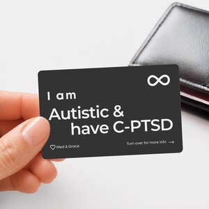May include: A rectangular black card with white text that reads I am Autistic & have C-PTSD. The card features an infinity symbol in the top right corner, a small heart icon next to the text Med & Grace, and the instruction Turn over for more info.