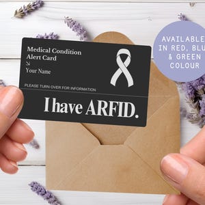 May include: A black medical alert card with white text and a white ribbon symbol is held in front of a brown envelope. The card reads "Medical Condition Alert Card" and "I have ARFID." A purple circle states "Available in Red, Blue & Green Colour."