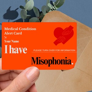 May include: An orange medical alert card with the text "Medical Condition Alert Card" and "I have Misophonia." A red heart and hands graphic is on the card. The card is held in front of a brown envelope.