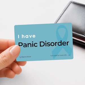 May include: A rectangular light blue medical alert card featuring the white text I have Panic Disorder, a light blue awareness ribbon, and the text Med & Grace. The card also includes the instruction Turn over for more info with an arrow.